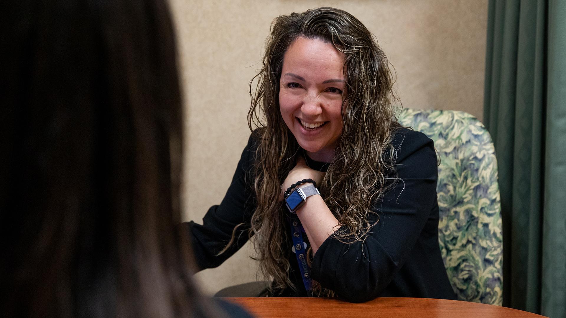 Dr. Amanda Steiman sits at a desk across from another woman who's back is to the camera and shoulder is in the frame. Dr. Steiman is smiling and interacting with the woman