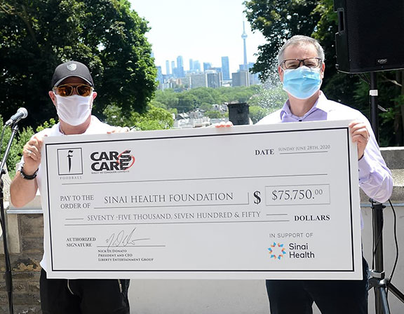 Two men wearing masks hold a presentation cheque for $75,750, made out to Sinai Health Foundation