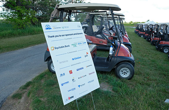 Rows of red golf carts sit in the background behind a poster with event sponsors listed.