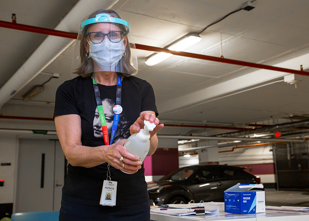 Screener with a mask and shield holding a hand sanitizer bottle