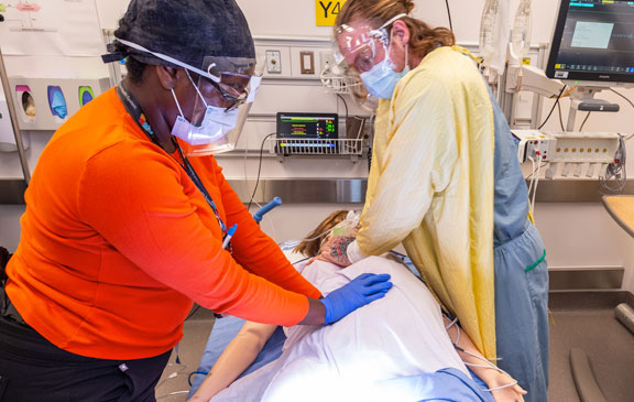 The emergency department health care providers in the simulation identify the mannequin is critically ill and perform CPR on the mannequin in the resuscitation room of the emergency department.