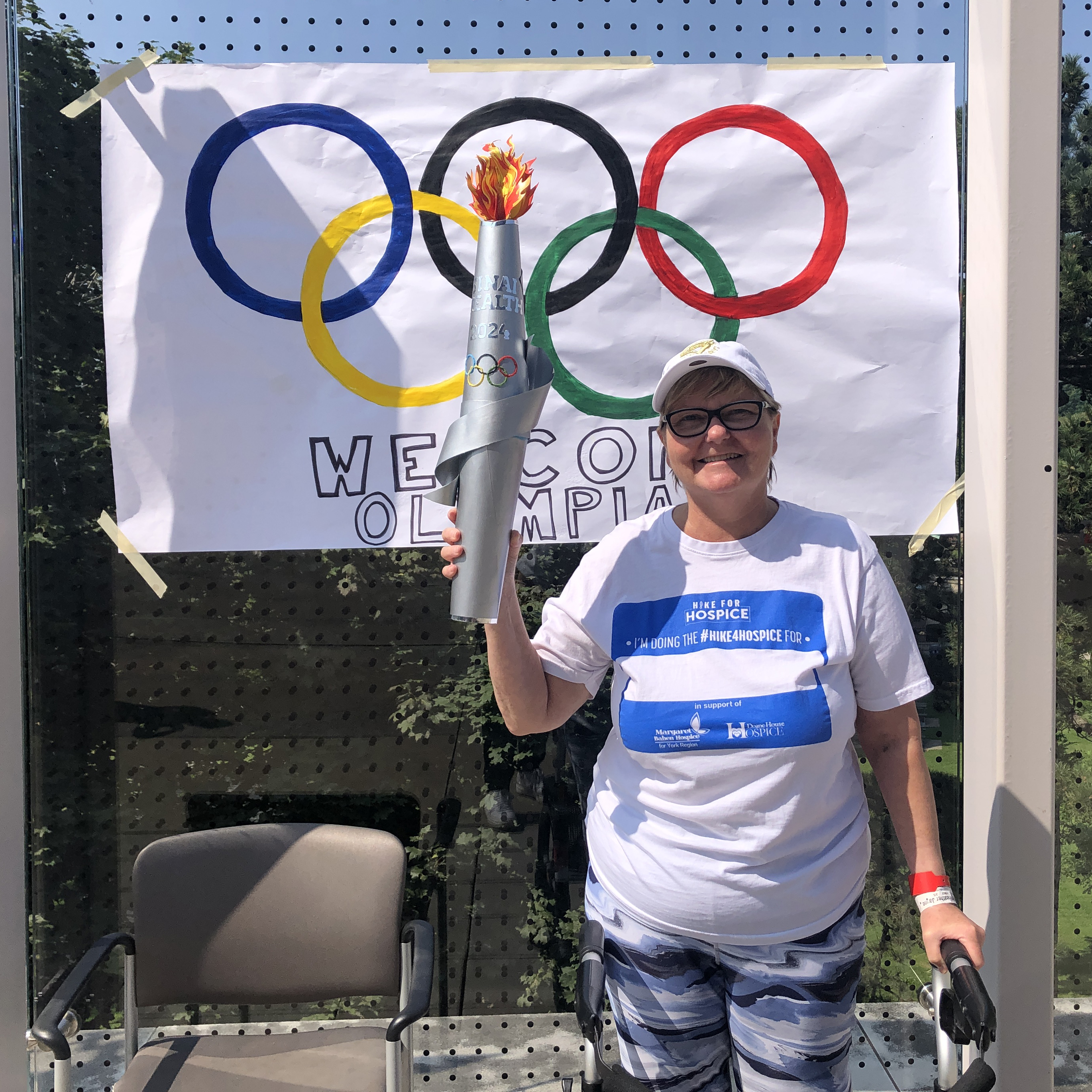 A patient from Hennick Bridgepoint Hospital holding a man-made olympic torch in front of an olympic sign 