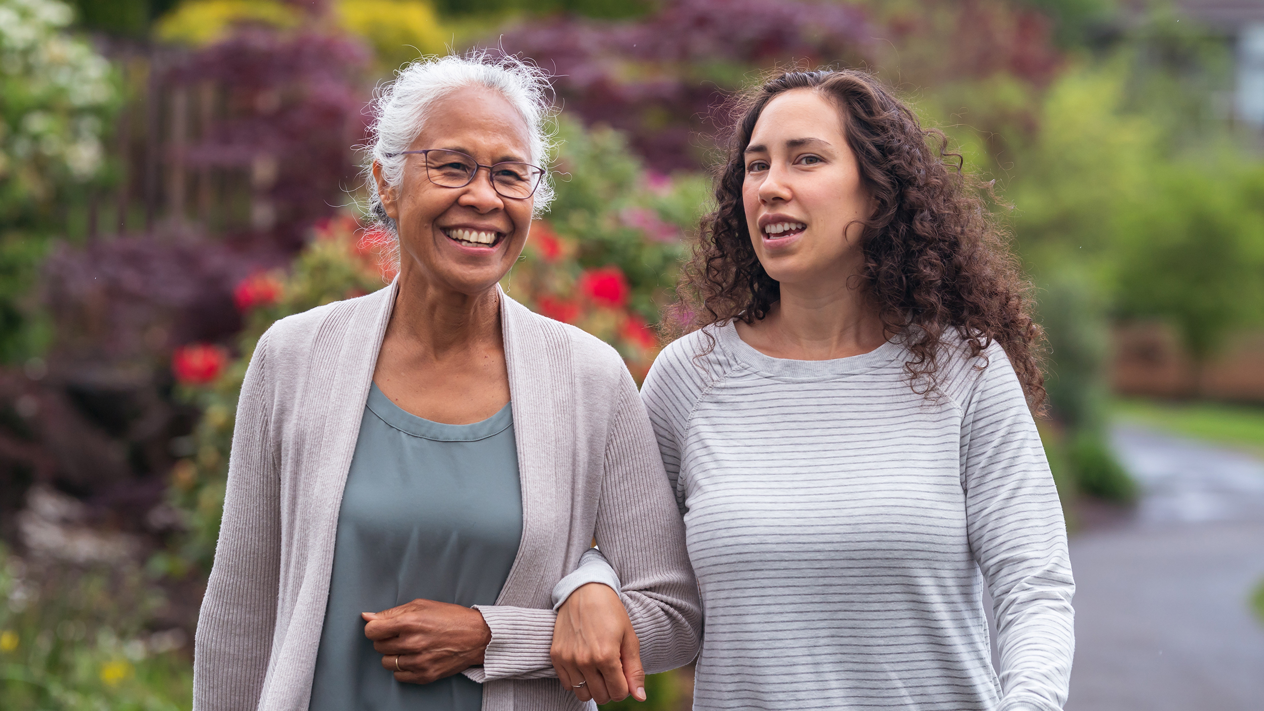 Mother and adult daughter walking arms linked in a park