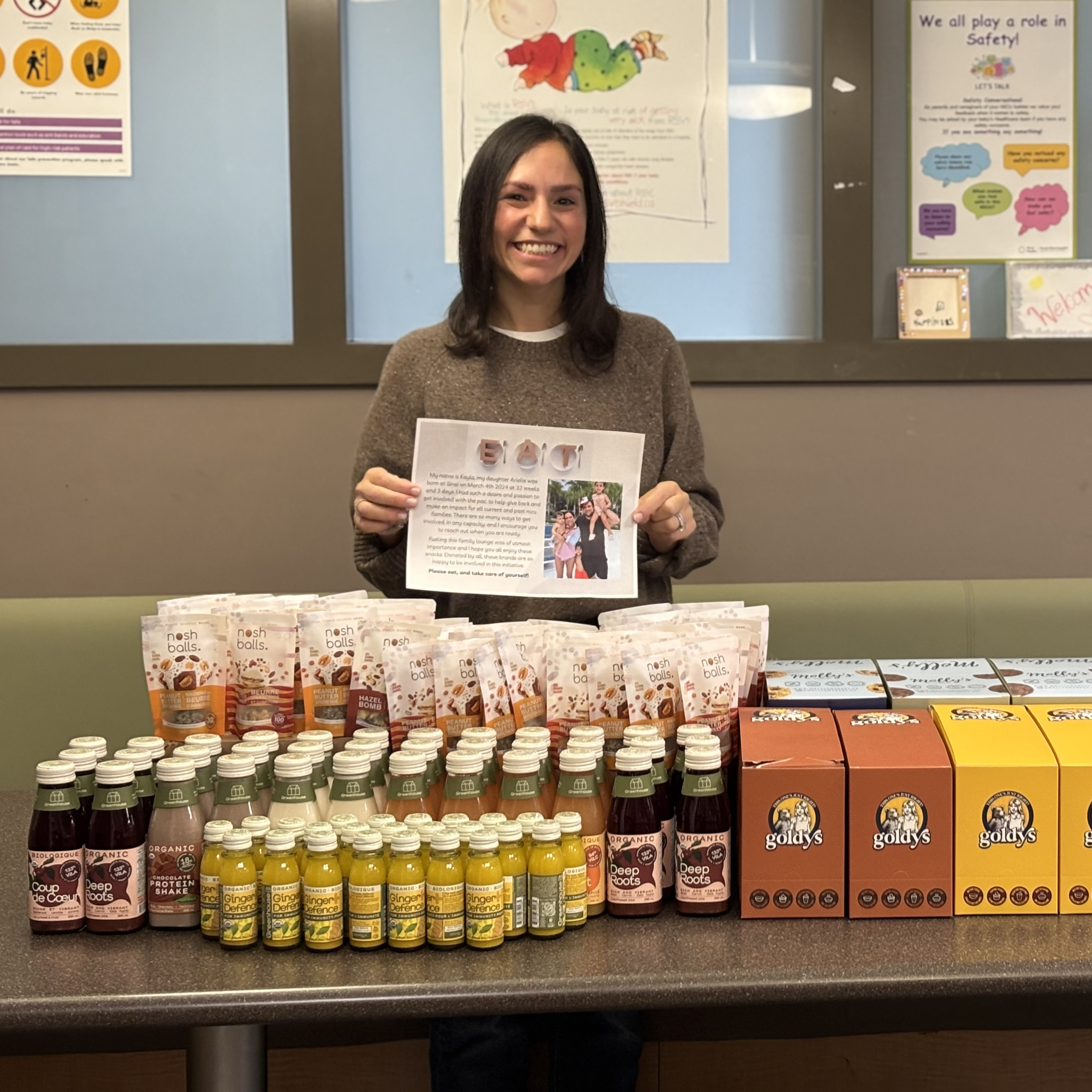 Mother from the Parent Advisory Committee standing behind a table full of various donated snacks for other parents at the NICU.