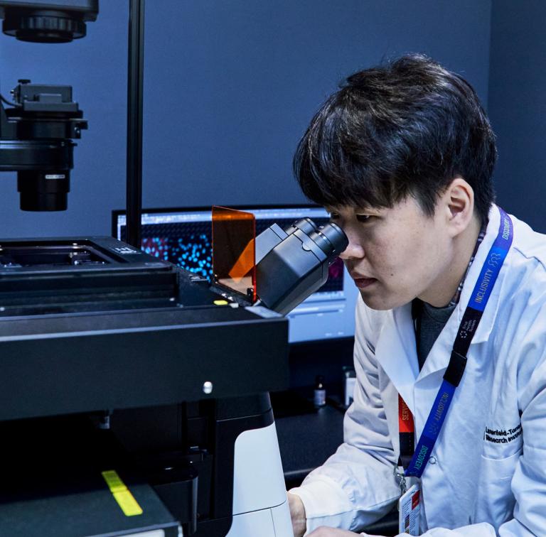 Man in a lab coat looking into a microscope in a laboratory