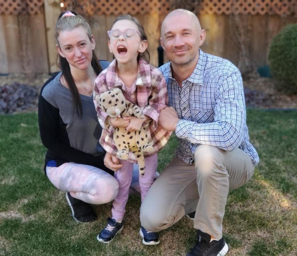 Mother and father kneel on the ground next to child