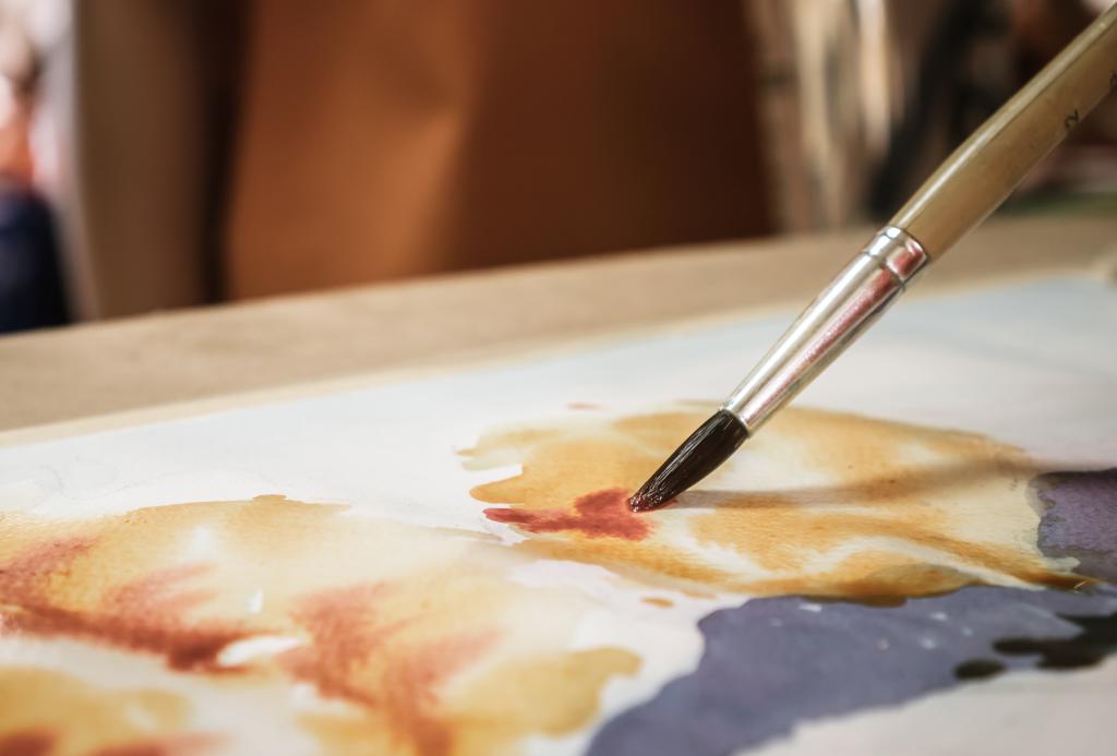 A paintbrush adds red paint to a water colour painting