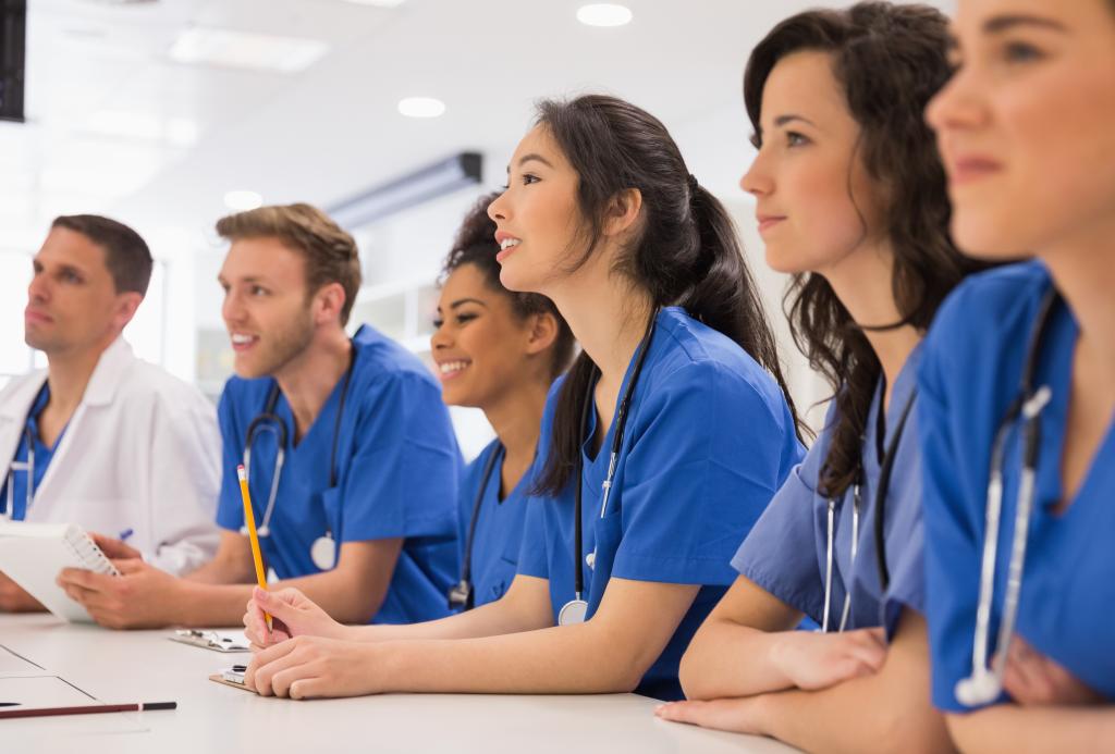 A group of people in scrubs sits at a table in a classroom