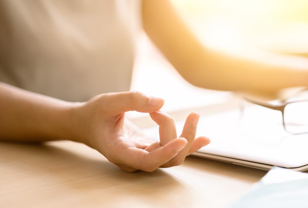 The hands of a person sitting at a desk meditating in front of a closed laptop