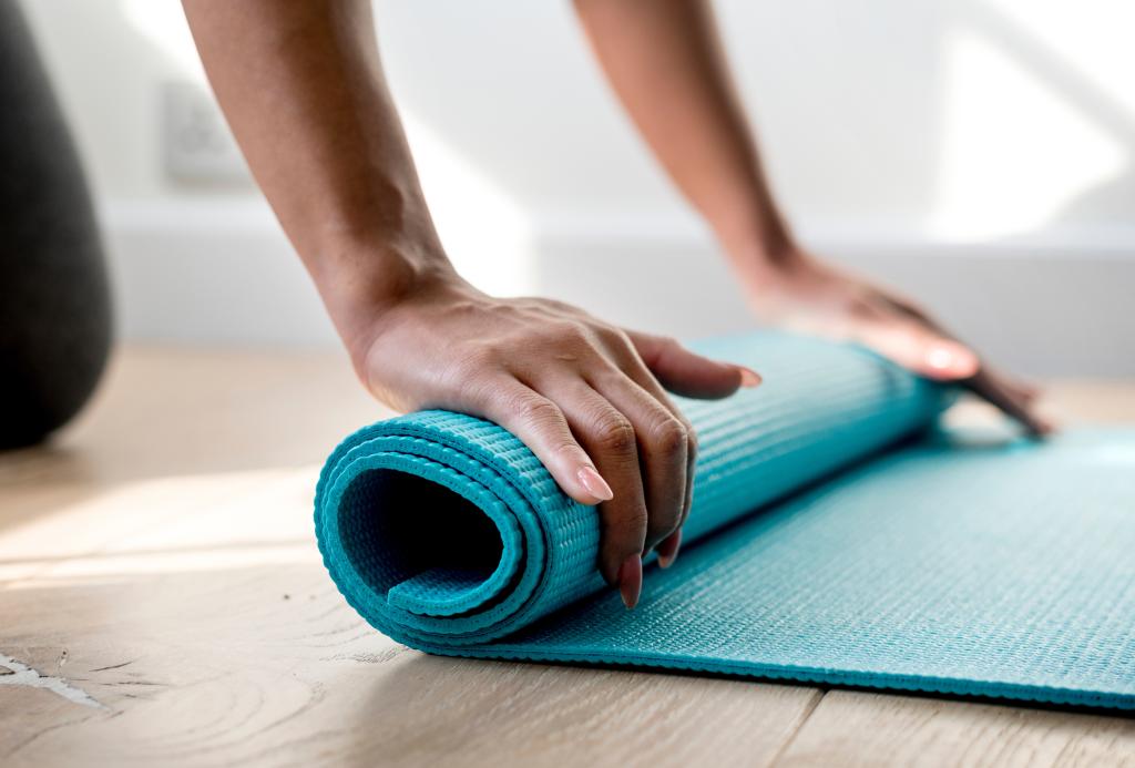 The hands of a person rolling up a blue yoga mat