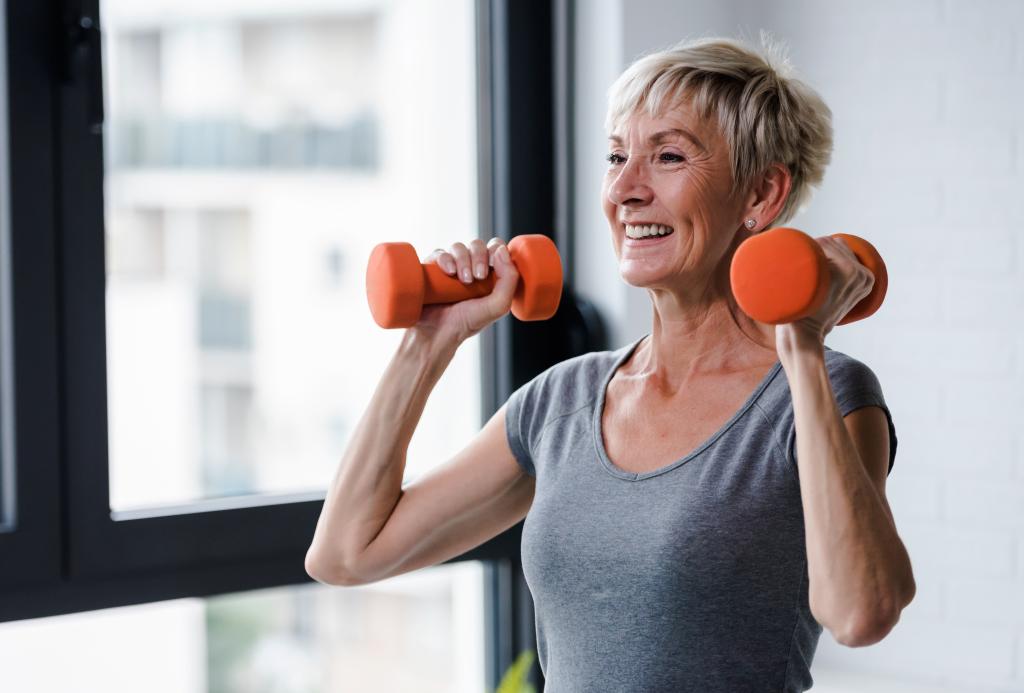 A woman lifts two orange dumbbells