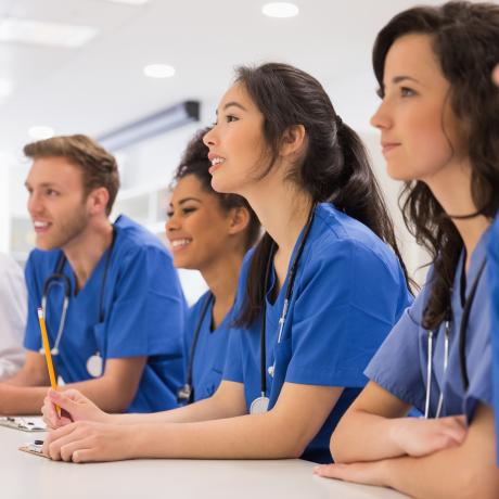 A group of people in scrubs sits at a table in a classroom