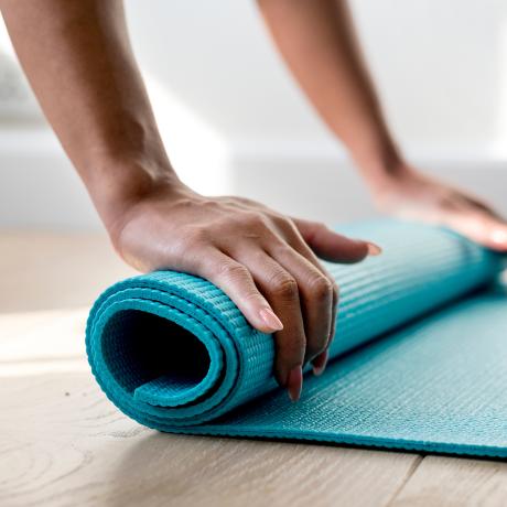 The hands of a person rolling up a blue yoga mat