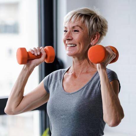 A woman lifts two orange dumbbells