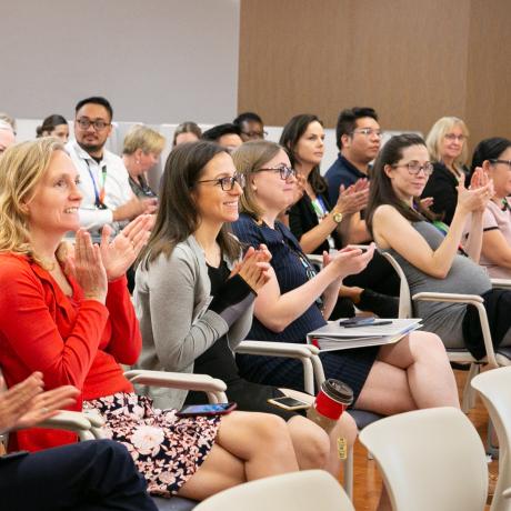 A group of people sits in an auditorium and applauds.