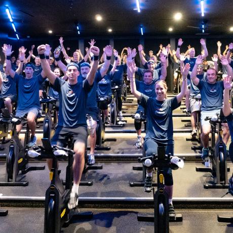 A group of people on spin bikes with their arms up in celebration