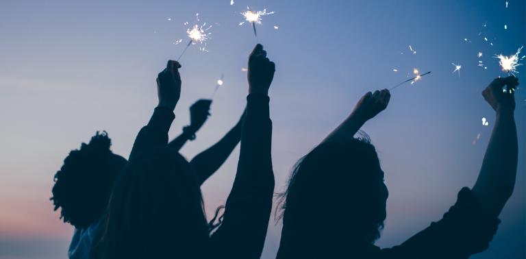 Silhouettes of people waving sparklers in the air outside