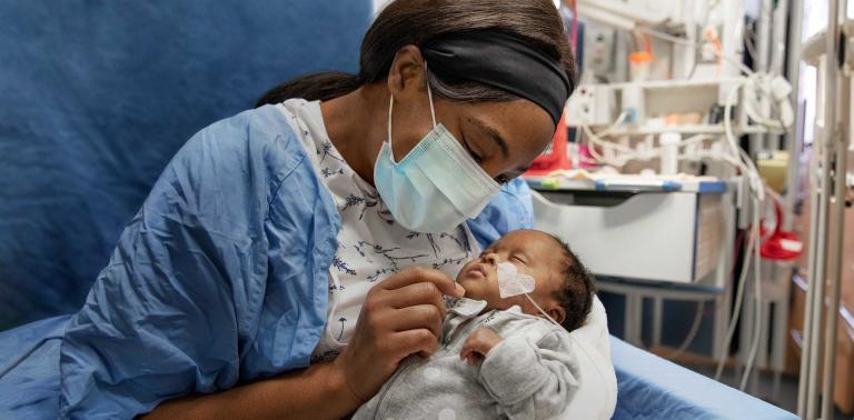 Baby being held by mother in blue hospital gown on blue chair