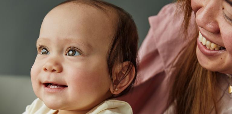 Baby smiling with mother behind her