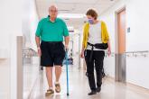 Patient walking with a cane. He is being assisted by a nurse.