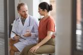 A male doctor and female patient sitting down and talking. The doctor is holding a tablet and explaining something.