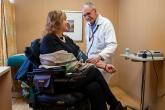 A urologist takes the blood pressure of a female patient in a wheelchair