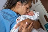 A woman sitting in a hospital bed kisses her newborn baby