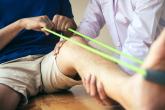 A physician assists a patient who uses an exercise band while sitting down