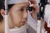 A woman undergoes an eye exam while leaning her face against ahead support