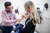 A physician examines a baby who is being held by her mother