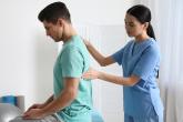 A healthcare provider assists a patient sitting on an exercise ball