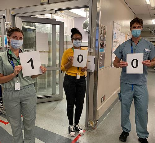 Three hospital staff holding up signs spelling out the number 100"