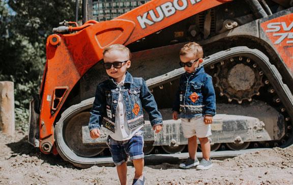 Toddler twins standing in front of a small construction vehicle