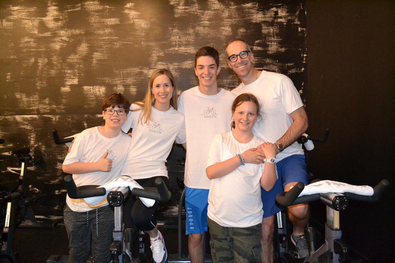 Man and woman sit on exercise bikes. Three children stand beside them. 