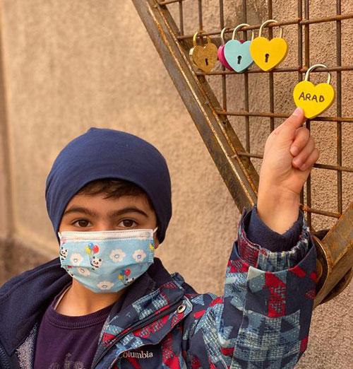 A child wearing a coat and a medical mask holds a heart-shaped lock