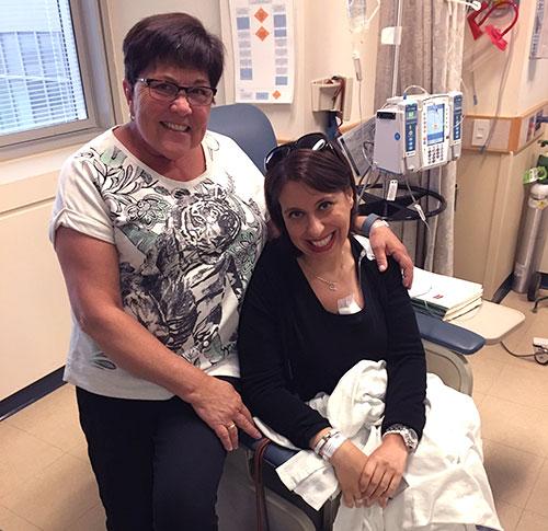 Two smiling women sit on a treatment chair.