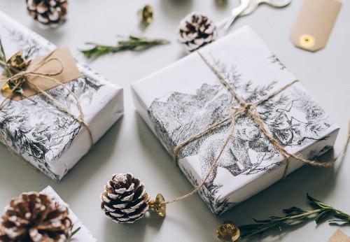 Holiday gifts wrapped in white paper and twine, surrounded by pinecones and greenery.