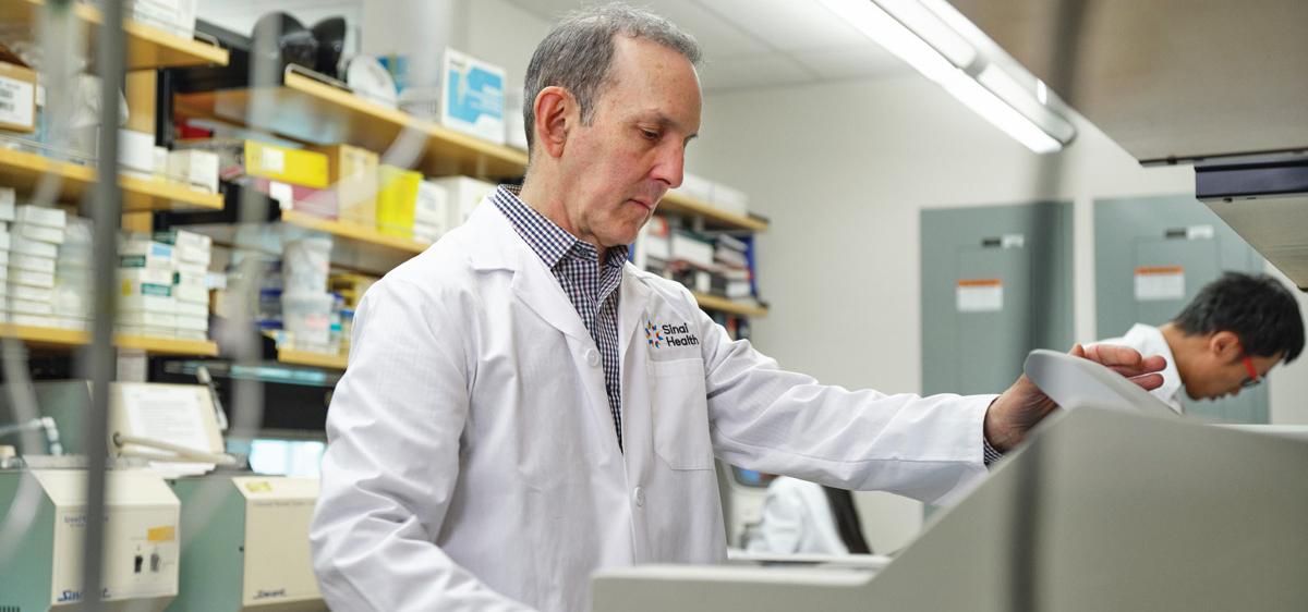 Dr. Daniel Drucker operating a lab instrument. He is wearing a white lab coat