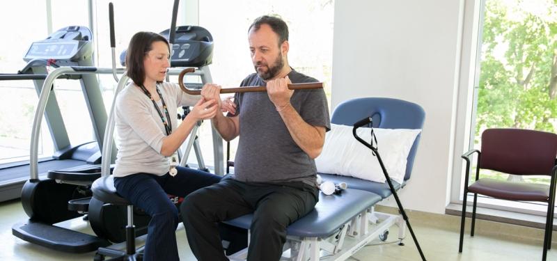 Physician helping man lift cane with both hands at rehabilitation centre. 