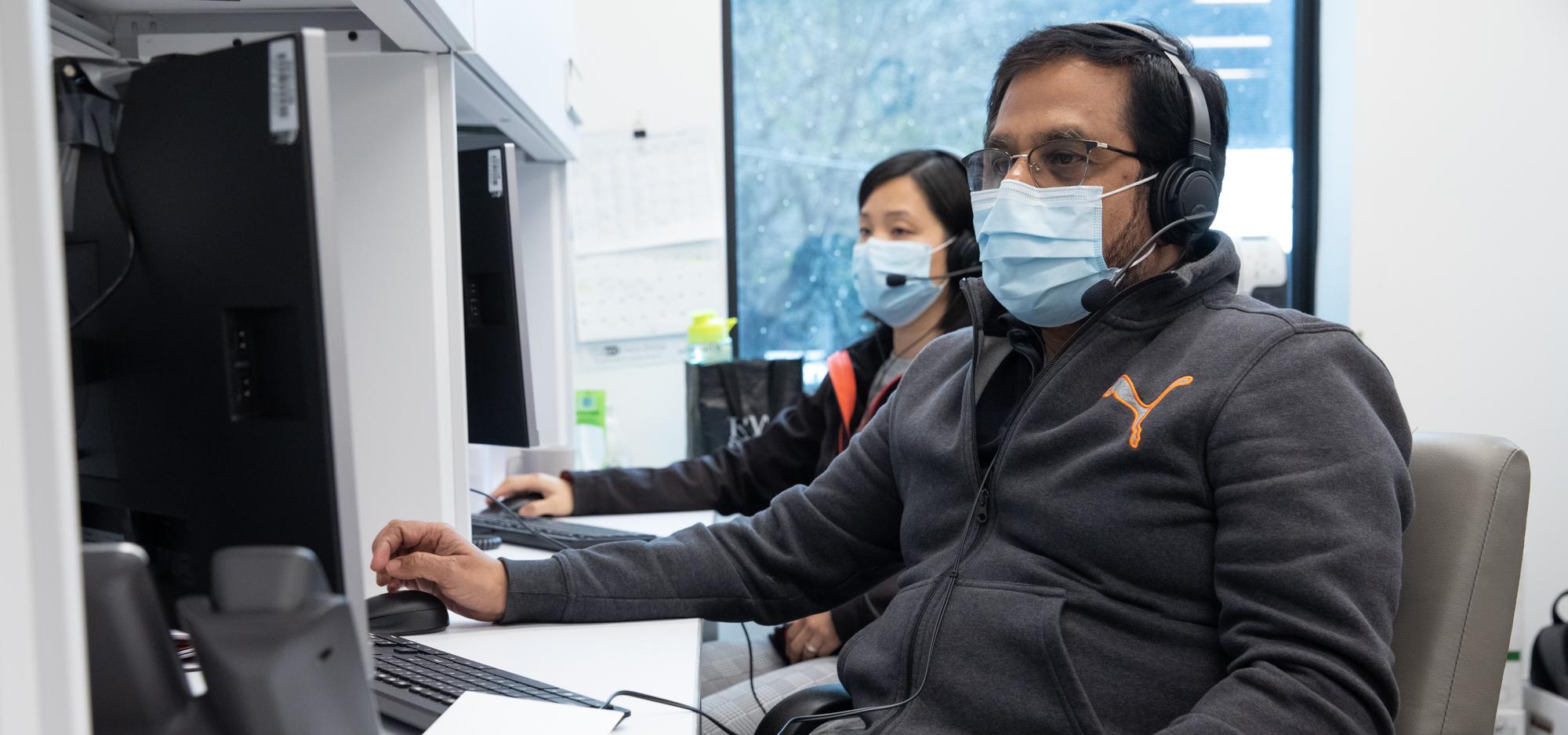 Two individuals wearing facemasks using computers