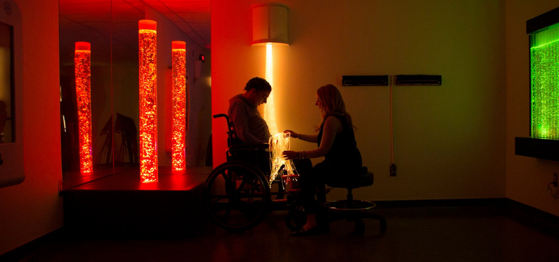 Woman sitting with person in wheelchair in dimly lit room with lights.