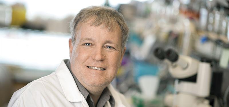 Man in lab coat in front of a microscope.