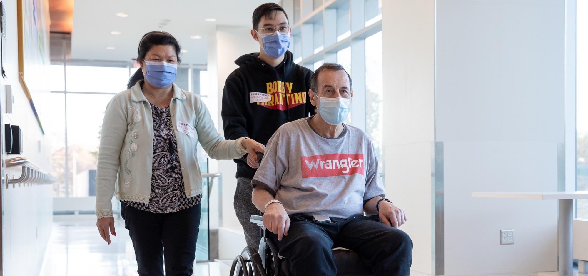 An older male in a wheelchair accompanied by his son and wife