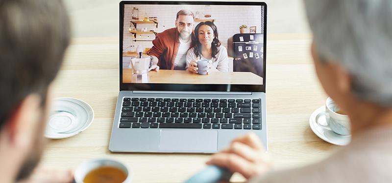 Two people using a laptop for a video chat with two other people. 