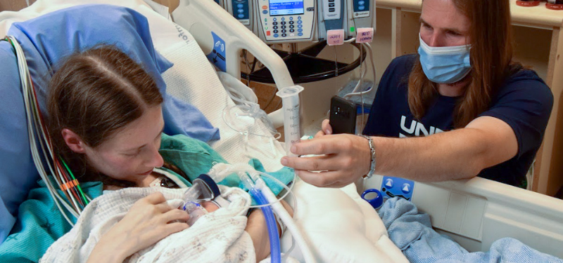 A woman and her baby in bed while a loved one is by her side