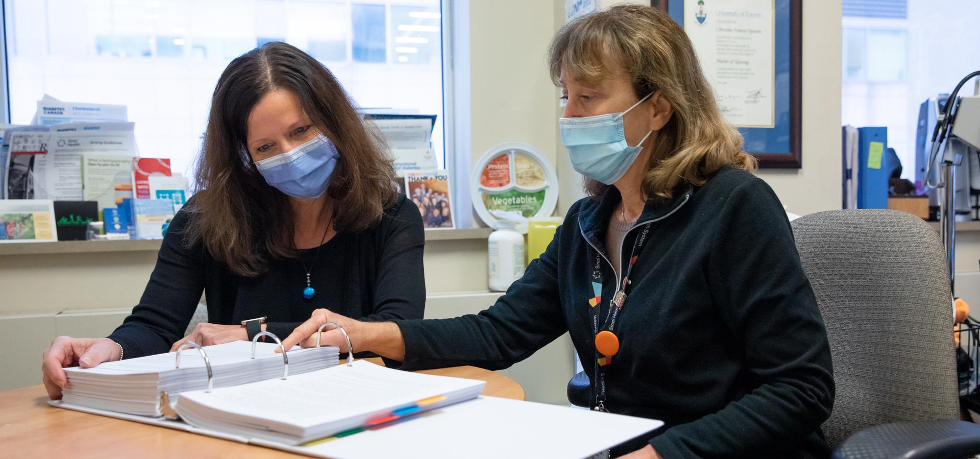 Two women wearing face masks sitting down together and reading