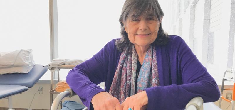 Mrs. Penn sitting in her hospital room smiling wearing a purple sweater.