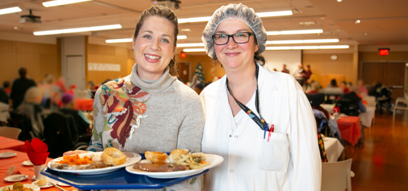 Two women with plates of food at the annual patient holiday meal event.