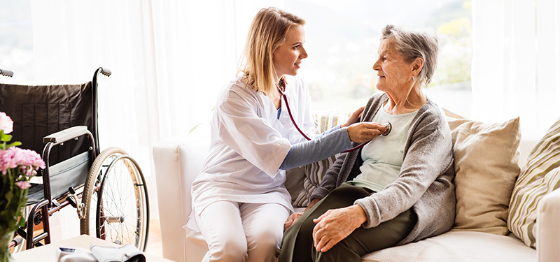 Woman listening to elderly woman's heart with stethoscope. 