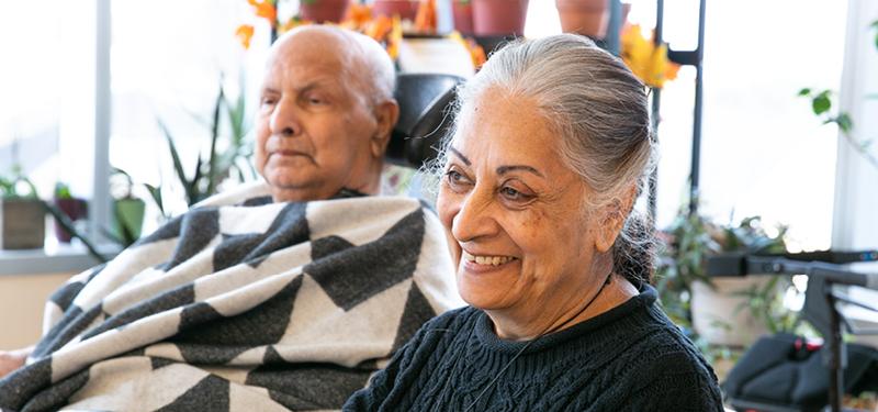 Female caregiver sitting beside elderly male, wrapped in a blanket